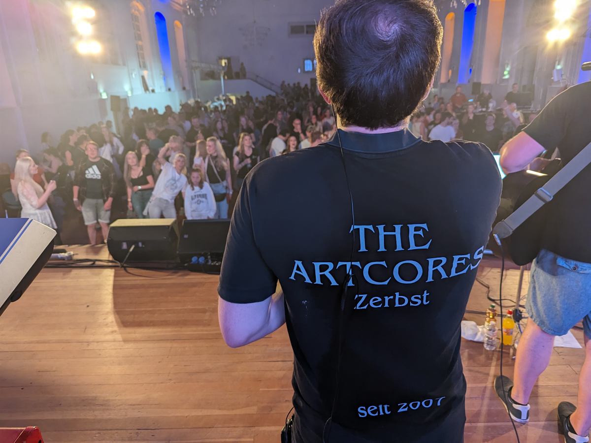 Rücken eines Musikers mit Aufdruck The Artcores Zerbst seit 2007, Blick ins Publikum