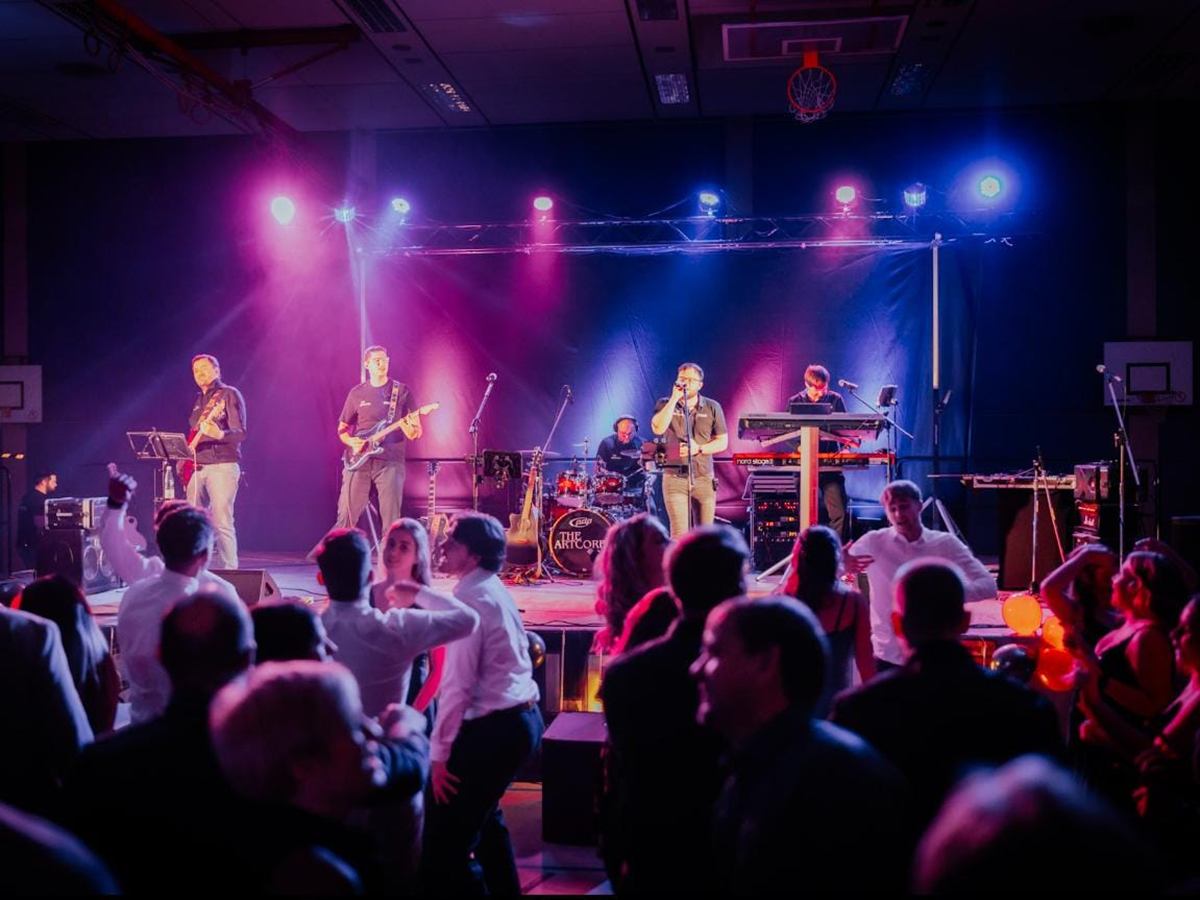 Band auf der Bühne in buntem Licht, im Vordergrund Gäste