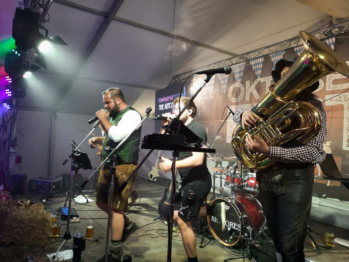 Sänger in Trachtenweste und Gitarrist auf der Oktoberfest-Bühne, dahinter das Schlagzeug mit The-Artcores-Logo