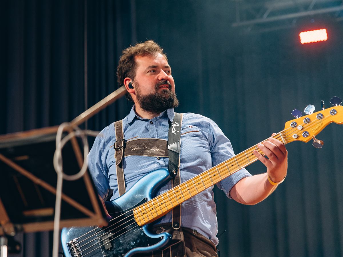 Bassist in Trachtenhemd und Hosenträgern spielt einen blauen Bass